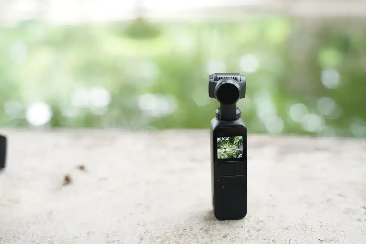 Compact pocket camera with dual lenses mounted on gimbal stabilizer, capturing mountain landscape footage.
