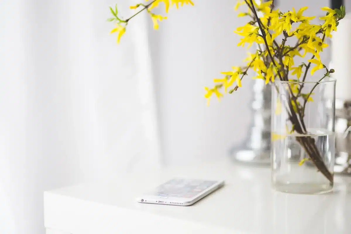 Desk by a sunny window with a smartphone showing translucent interface and a hand near a slider control