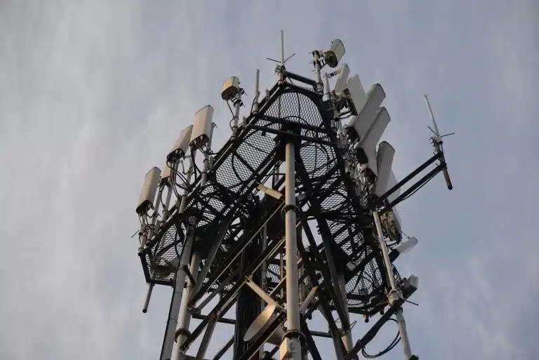Technicians hands adjusting a rooftop antenna with laptop and city skyline in daylight