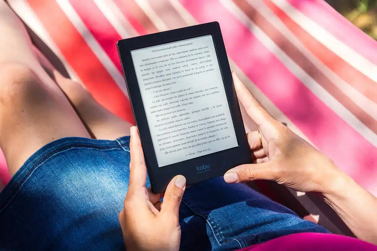 Person holding a slim e-reader in bright indoor daylight to show slimmer, lighter design