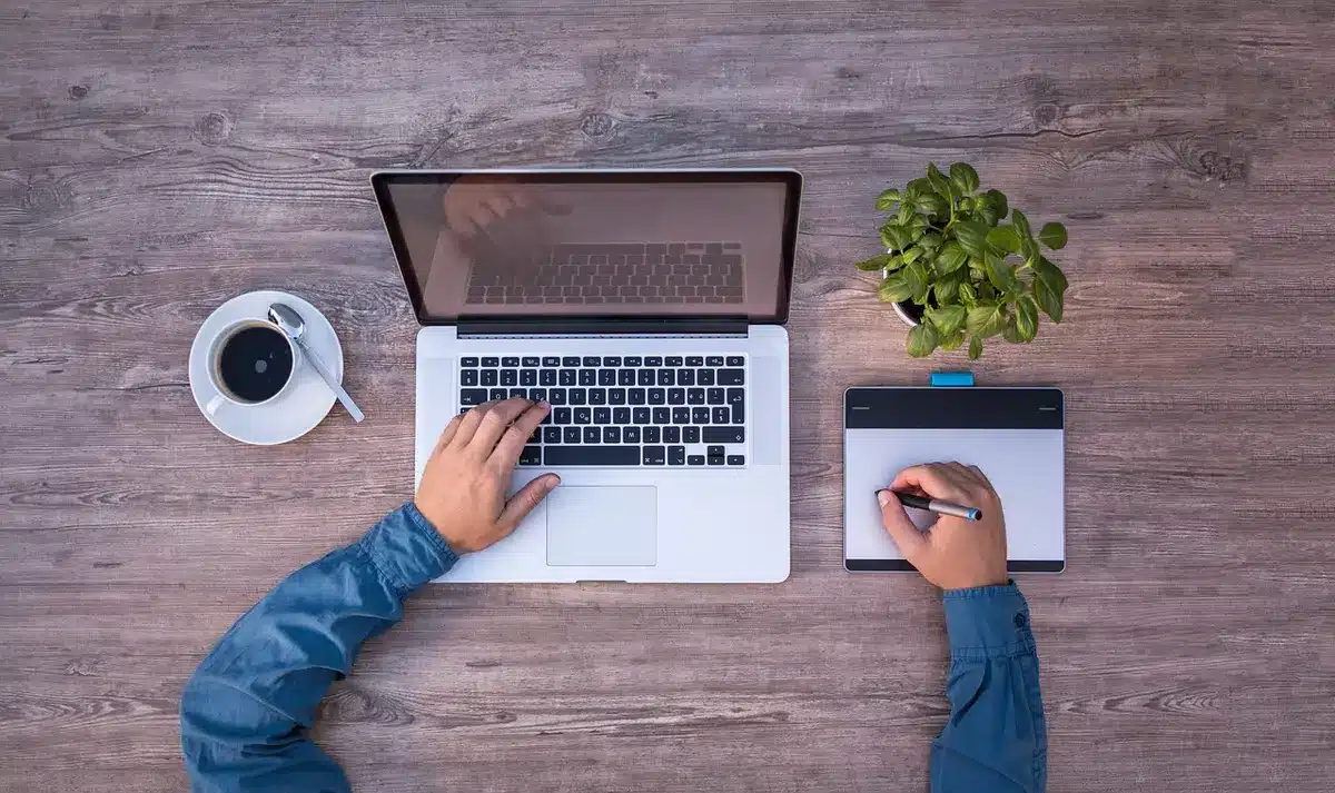 Two anonymous hands over a laptop showing code and UI mockups on a canvas