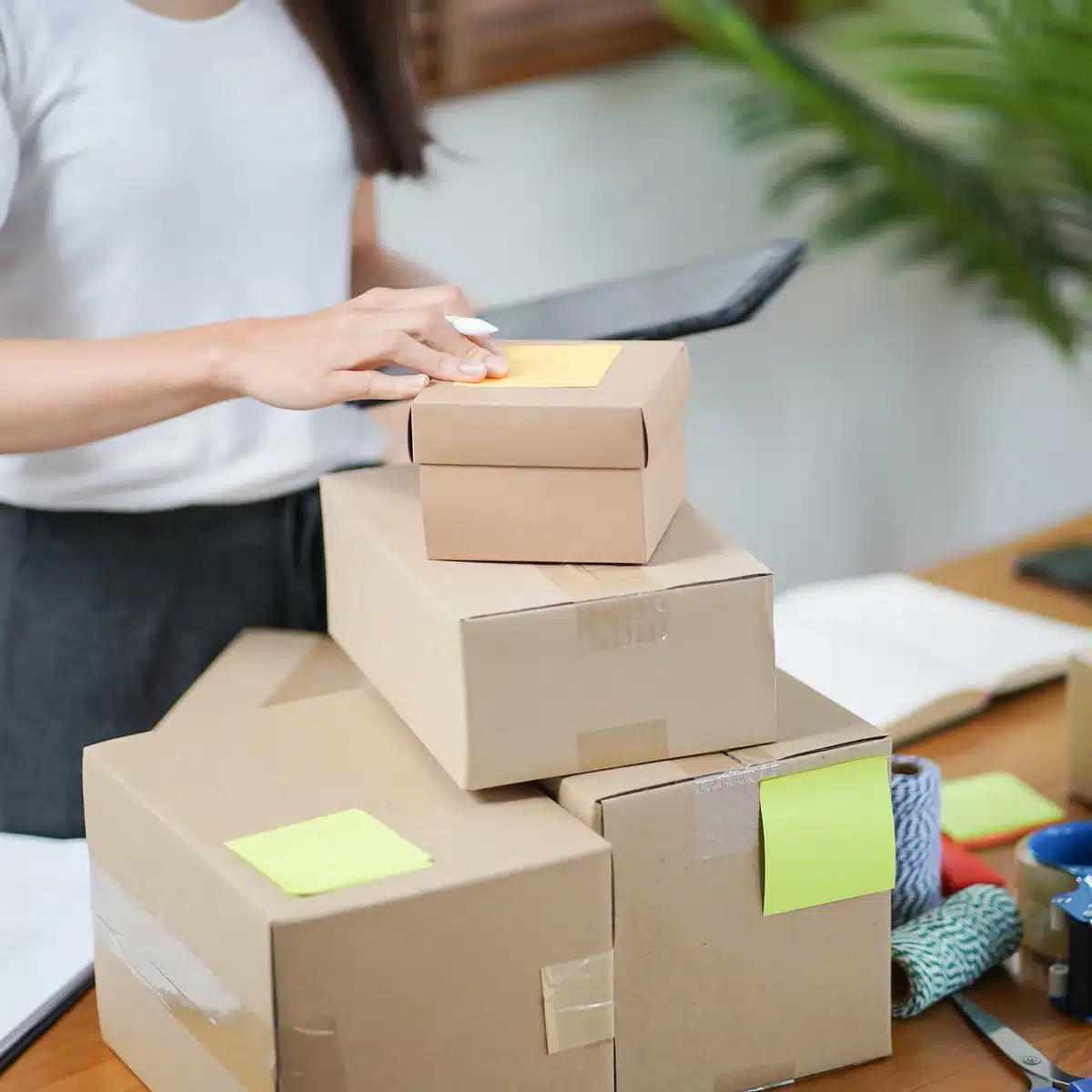 Hands packing a takeaway box beside a tablet showing delivery orders in a bright small restaurant kitchen