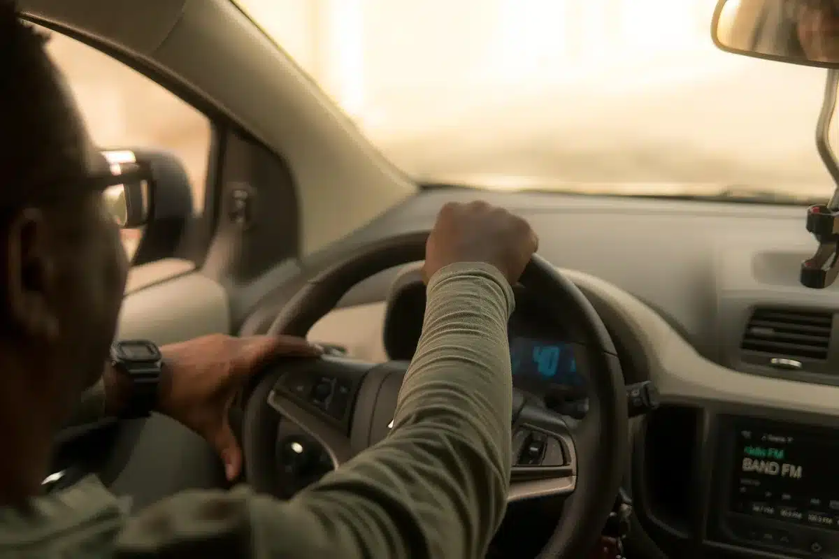 Hands on steering wheel with wet road visible through the windshield