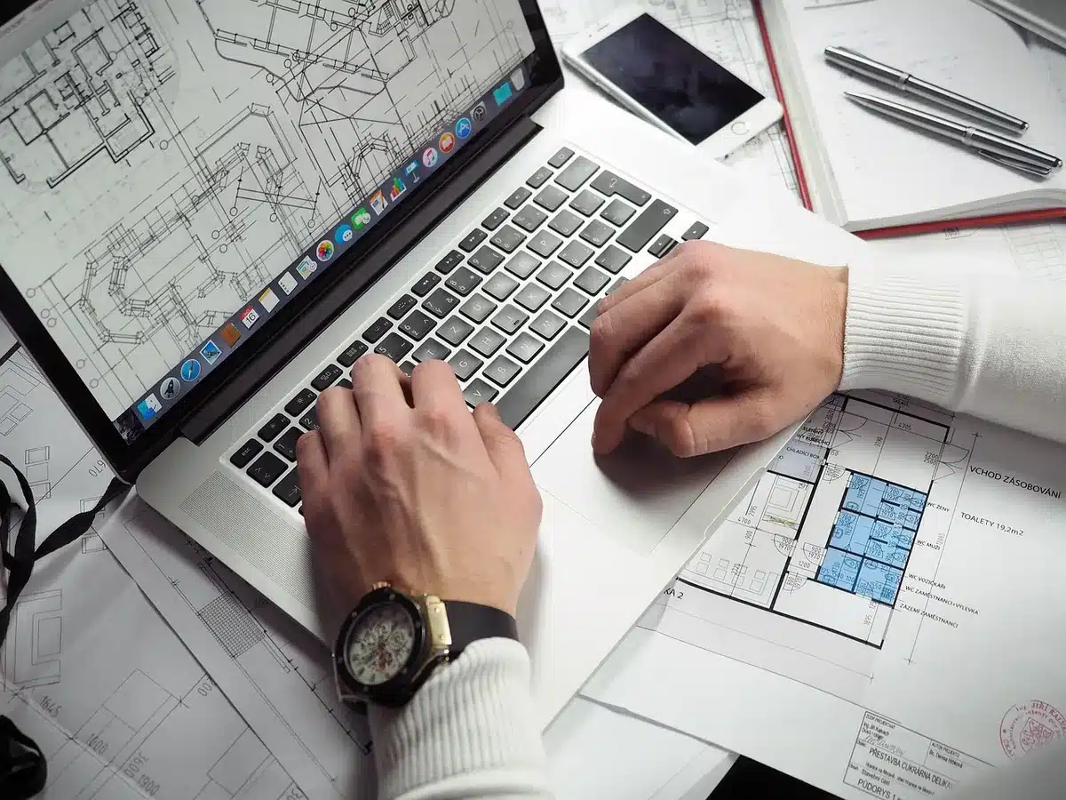 Person at a sunlit desk using a smartphone with settings open beside a closed laptop